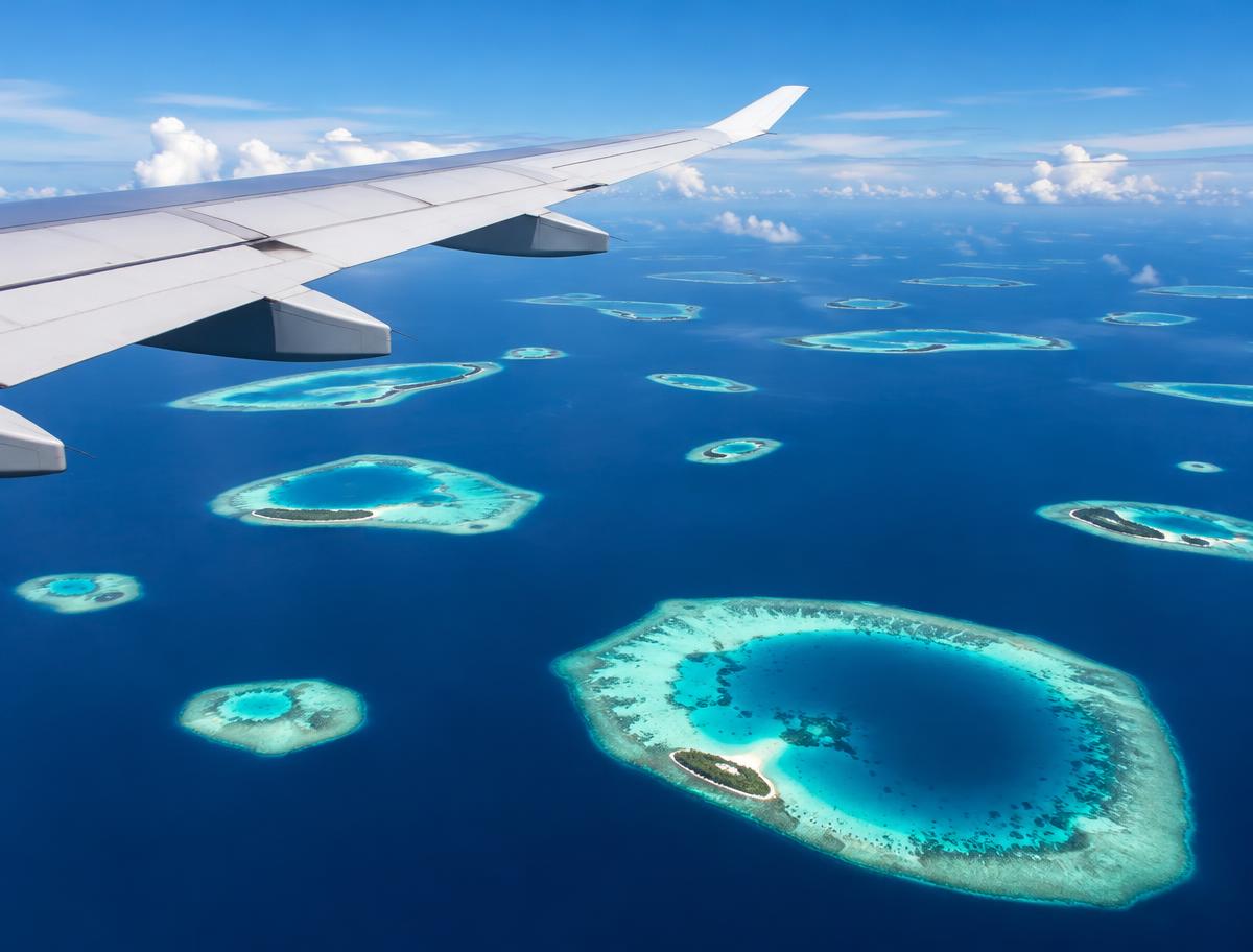 Airplane wing above scattered Maldives atolls and turquoise lagoons
