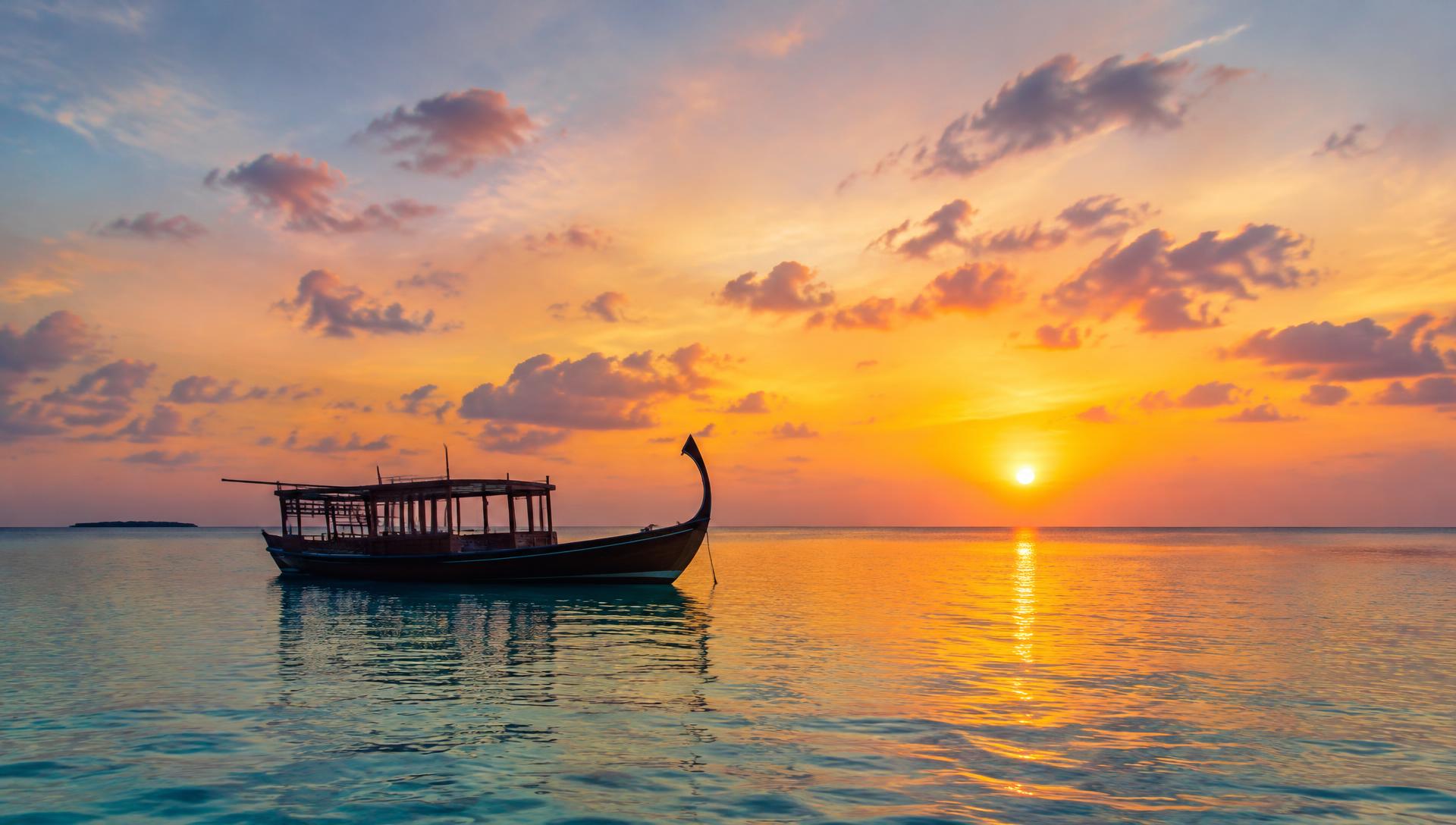 A traditional Maldivian dhoni boat on calm water at sunset